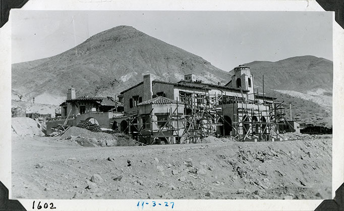 This is an historic black and white photograph from the Scotty's Castle Historic Photograph Collection, Death Valley National Park of Scotty's Castle Main House and Annex, looking northeast. Enclosed Patio west wall stuccoed. Annex west end stuccoed and tile roofing nearly complete. Main House exterior walls stuccoed. Solarium roof tiled. Scaffold off Observation Tower. December 3, 1927. Photographed by Mat Roy Thompson.