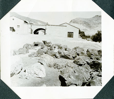 This is an historic black and white photograph from the Scotty's Castle Historic Photograph Collection, Death Valley National Park of Scotty's Castle Watercourse, looking east at Stables with gates open. Circa 1931.