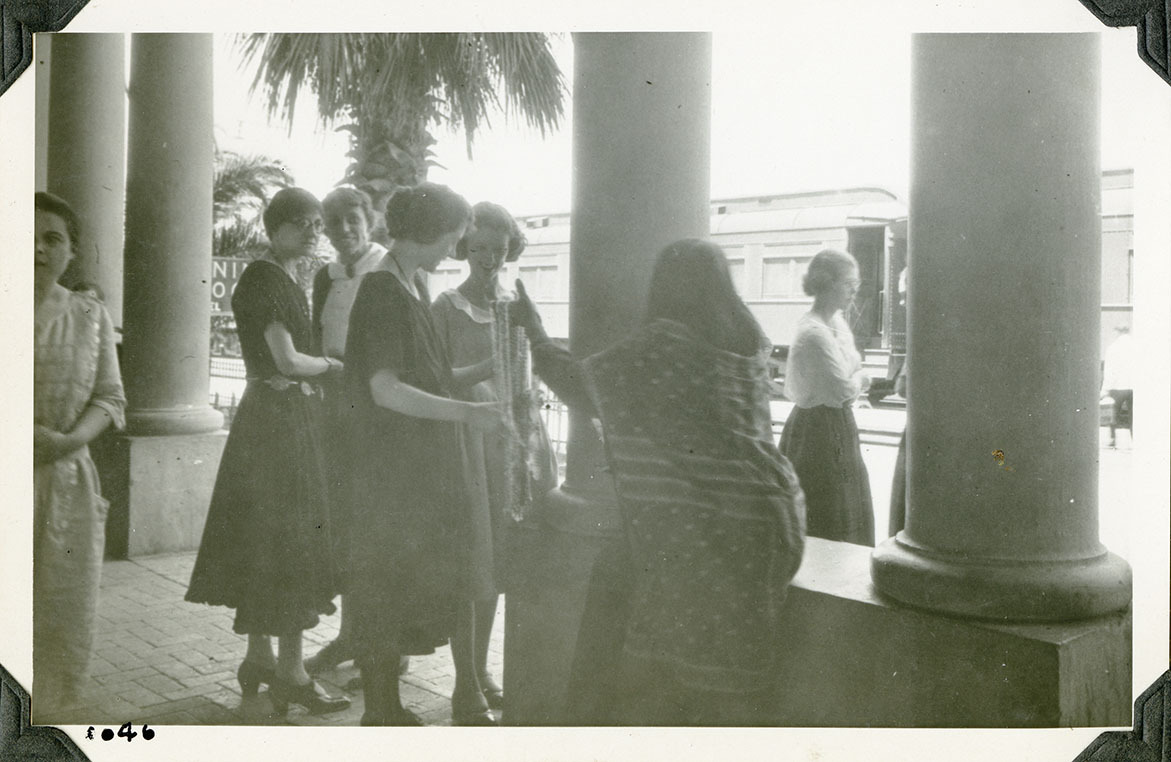 This is an historic black and white photograph from the Scotty's Castle Historic Photograph Collection, Death Valley National Park of several women looking at something a woman is holding up for sale. Number in black ink in lower left corner.