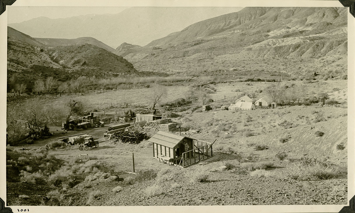 This is an historic black and white photograph from the Scotty's Castle Historic Photograph Collection, Death Valley National Park of Upper Grapevine Ranch looking down Grapevine Canyon. Cluster of tents built in 1917 before permanent structures begun. Circa 1919, base on the year Albert M. Johnson took or had someone else take many photographs.