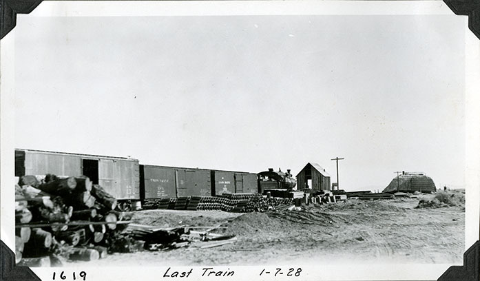 This is an historic black and white photograph from the Scotty's Castle Historic Photograph Collection, Death Valley National Park of materials off loaded from Tonopah and Tidewater Railroad train. Last train to run on line north of Beatty, Nevada, arriving at Bonnie Clare station. January 7, 1928. Photographed by Mat Roy Thompson.