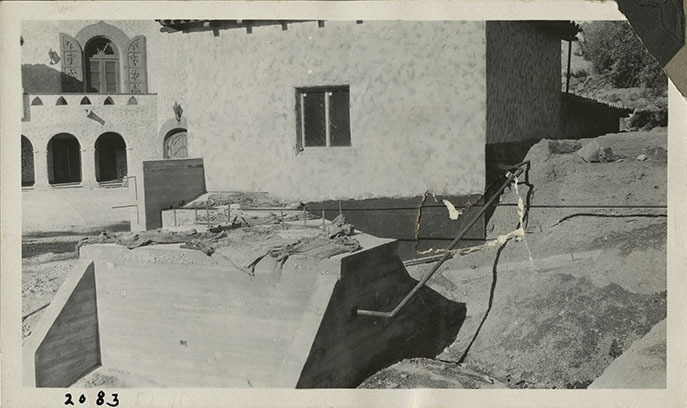 This is an historic black and white photograph from the Scotty's Castle Historic Photograph Collection, Death Valley National Park looking northwest at Scotty's Castle Gas House under construction. Scotty's Castle Annex in background. Circa 1930. Photographed by Mat Roy Thompson.