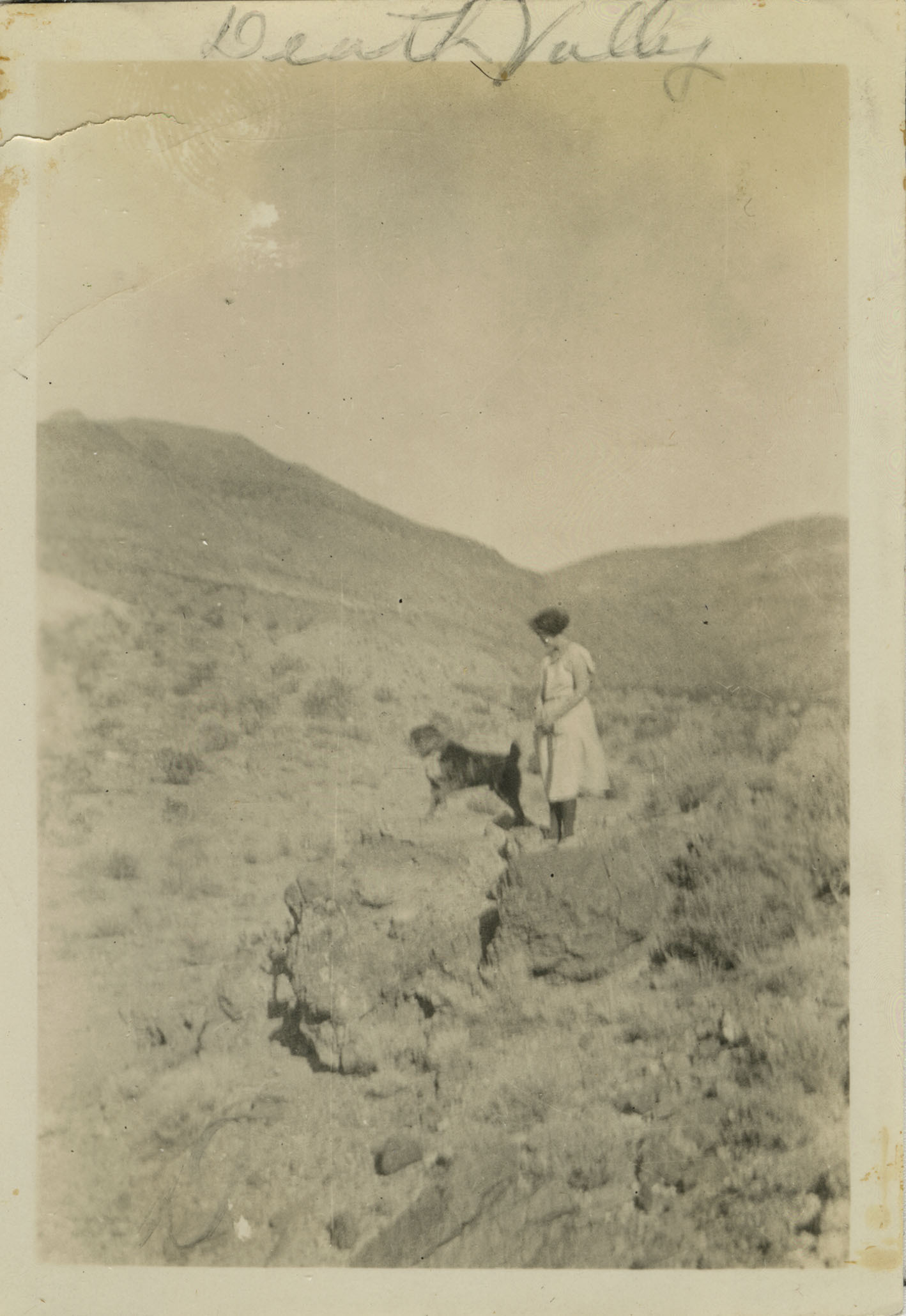This is an historic black and white photograph from the Scotty's Castle Historic Photograph Collection, Death Valley National Park of Melba Kropf with dog Bob on a walk, Death Valley Ranch. Circa 1923.