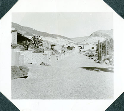 This is an historic black and white photograph from the Scotty's Castle Historic Photograph Collection, Death Valley National Park of road looking east to Scotty's Castle Stables between Hacienda and Watercourse landscaping. Circa 1931.