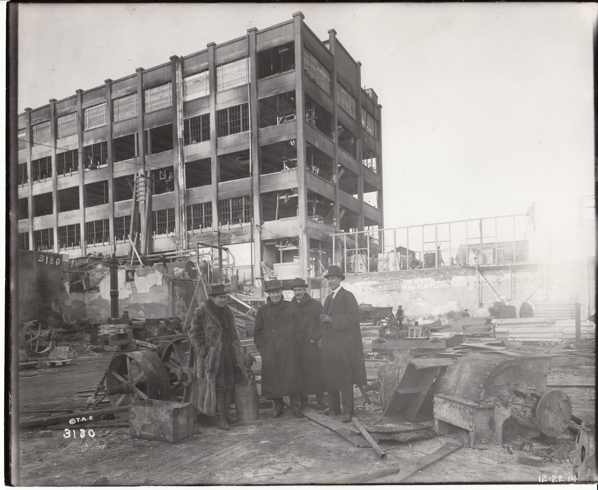 Charles Edison, Thomas Edison, C. H. Wilson and an unidentified man standing in the yard after the fire, Building 24 in the background.