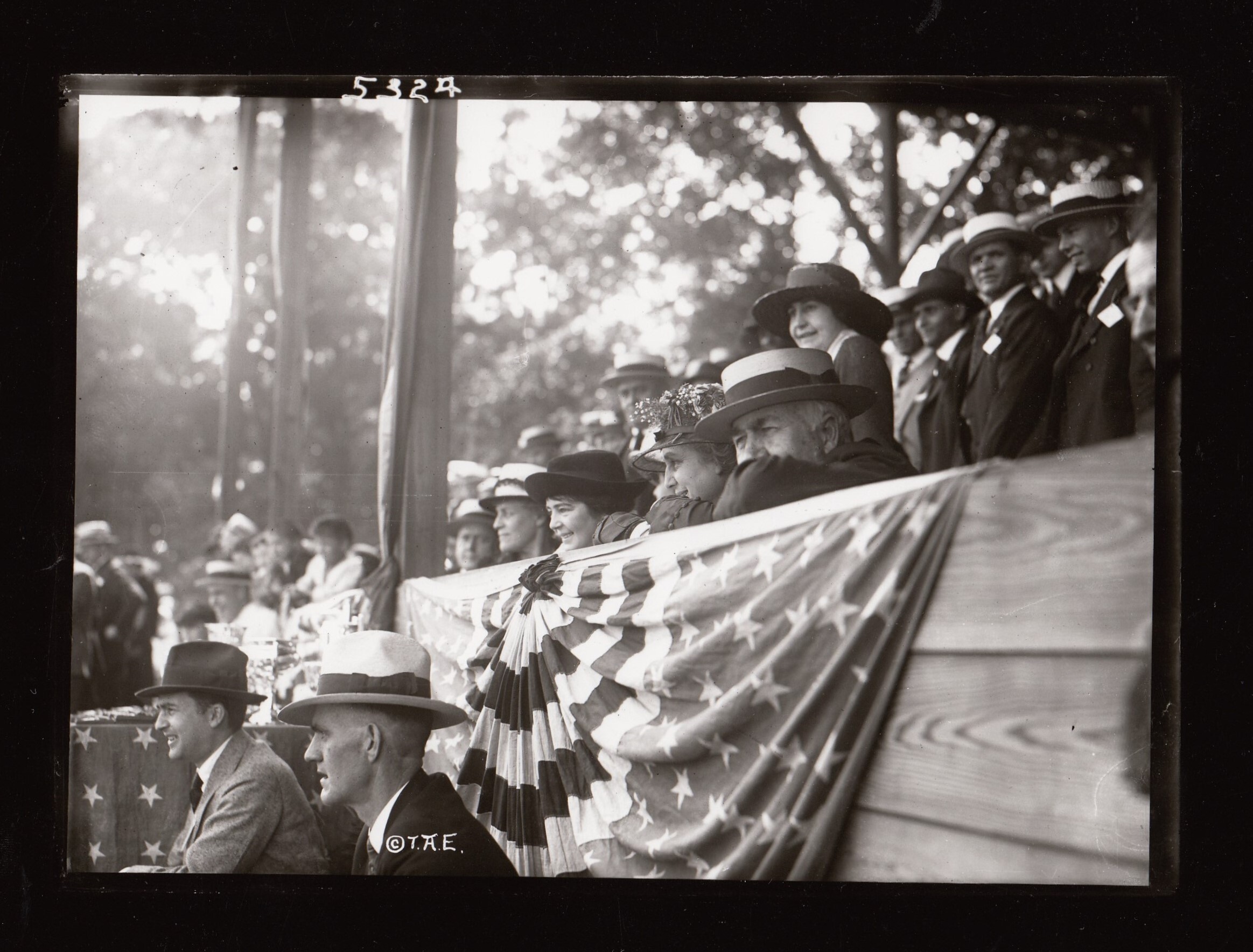 Thomas Edison and Mina Edison sitting in grandstand watching Edison field day activities at Olympic Park, Charles Edison in front of stands, Carolyn Edison next to Mina.