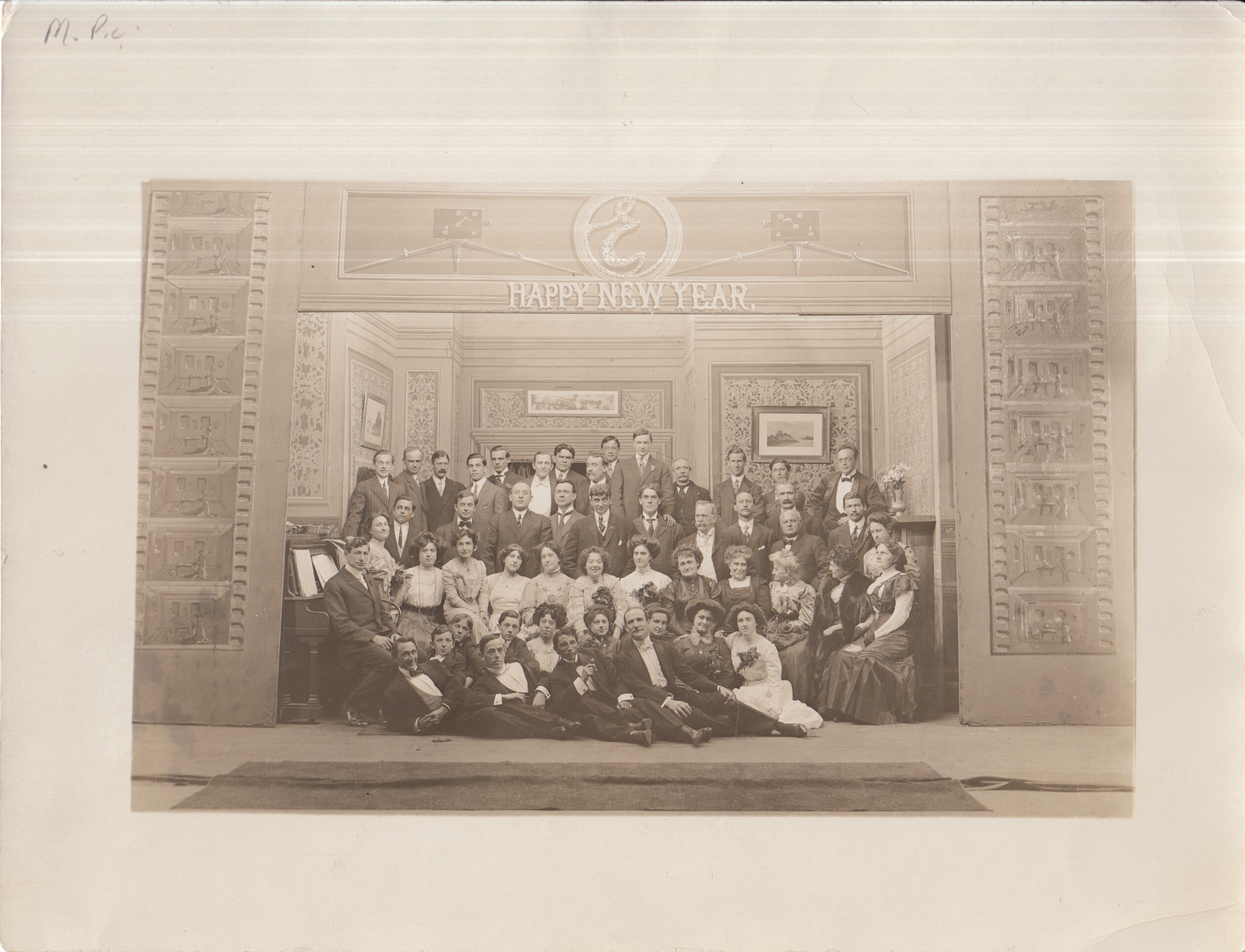 Group portrait of actors, directors, and cameraman. Text: Happy New Year" at top.