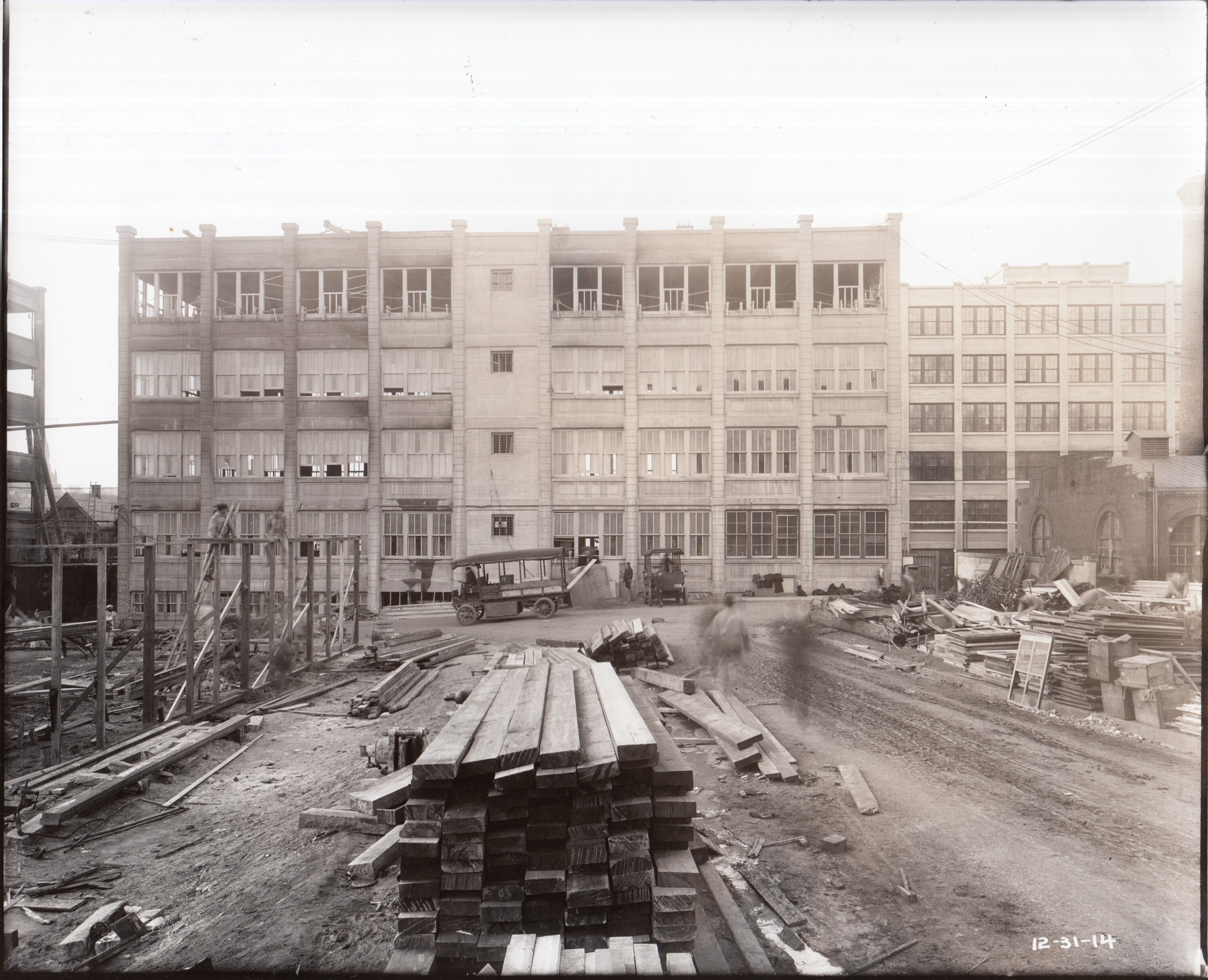 Building 25 viewed from yard, stack of lumber in foreground.