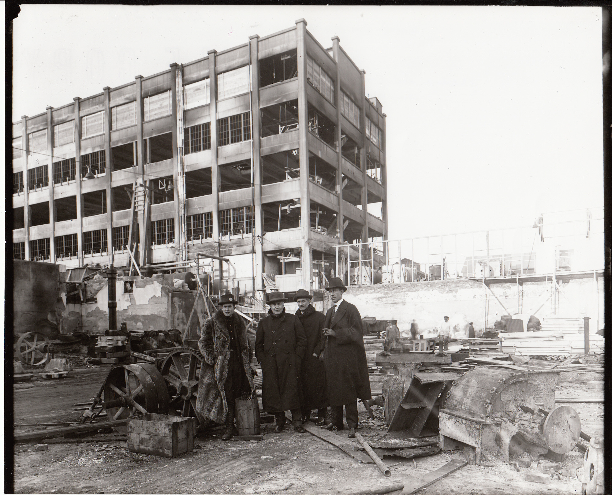 Charles Edison, Thomas Edison, C. H. Wilson and an unidentified man standing in the yard after the fire, Building 24 in the background.