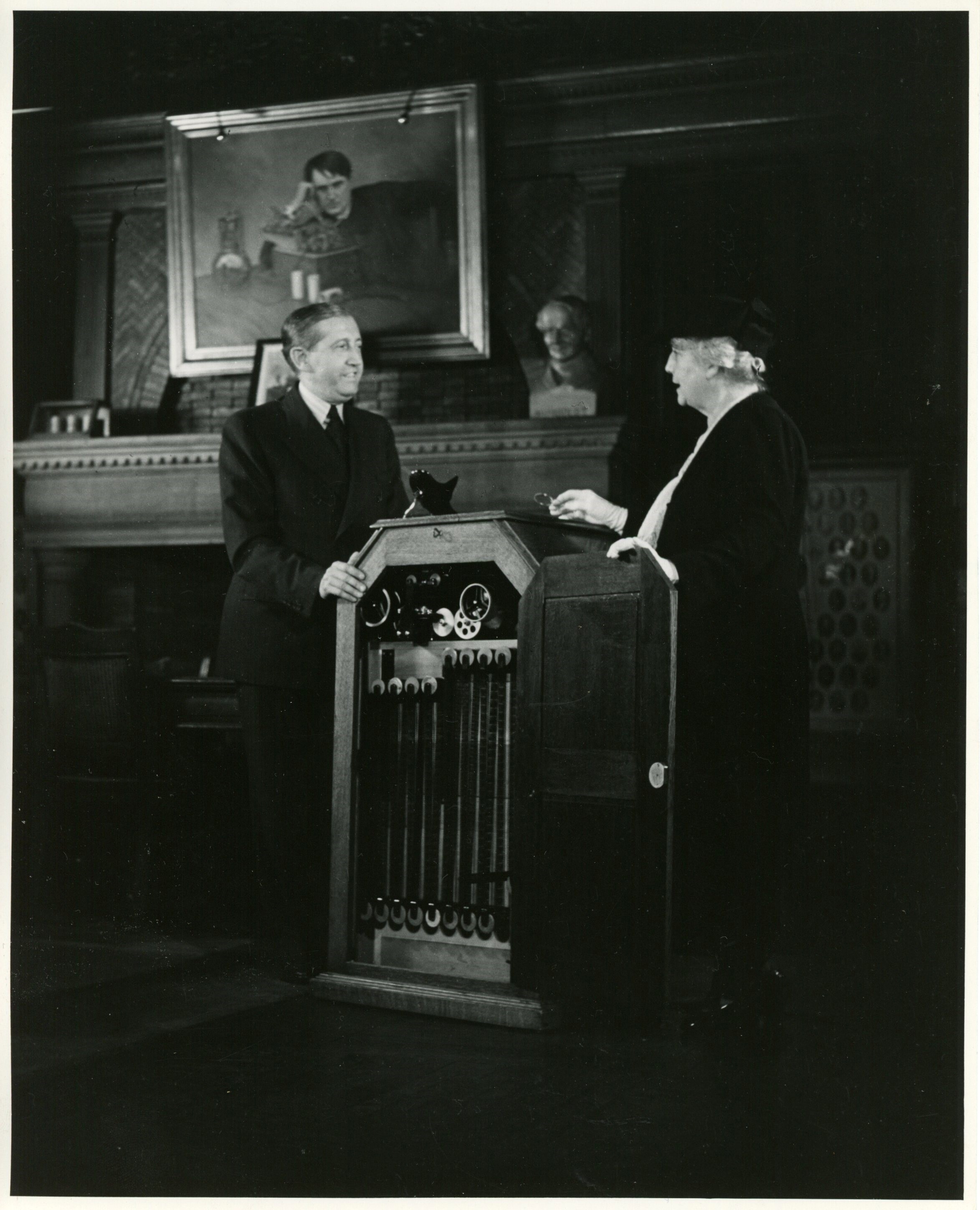 Will Hays and Mina Edison Hughes with peep-hole kinetoscope at celebration of fiftieth anniversary of motion pictures.