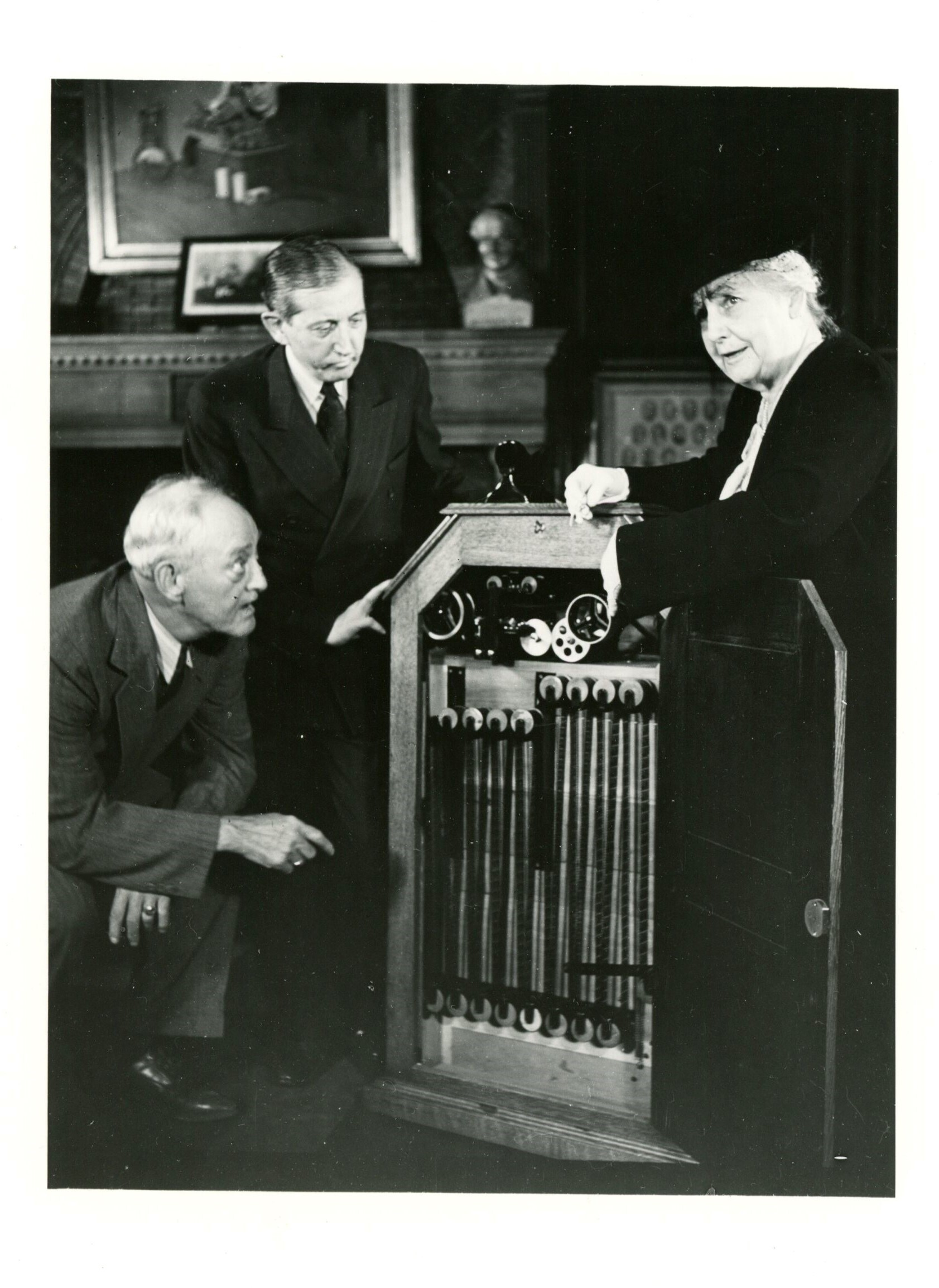 Will Hays, center, Mina Edison Hughes, and unidentified man with peep-hole kinetoscope at celebration of fiftieth anniversary of motion pictures.