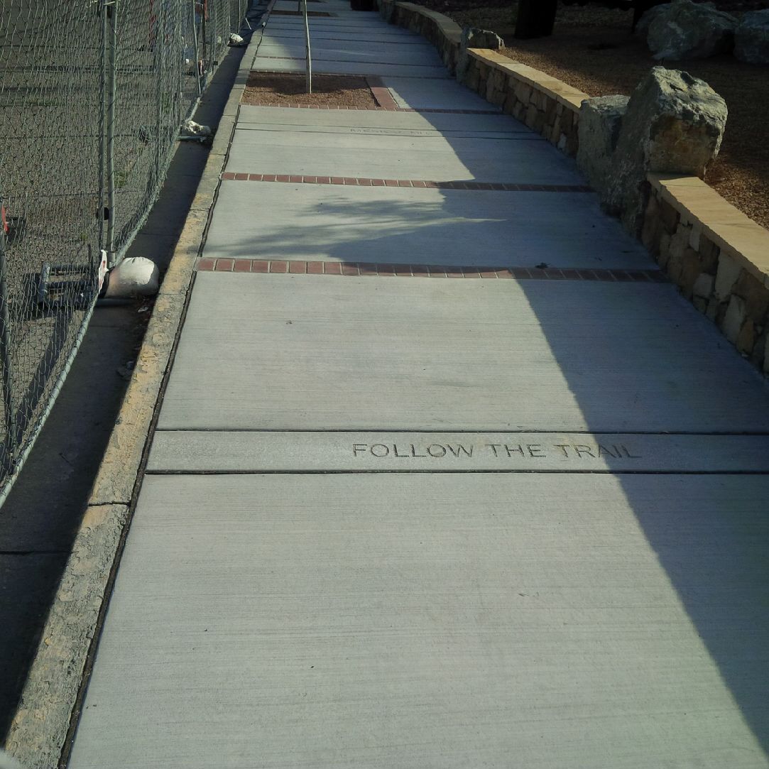 A sidewalk with a sign that says follow the trail.