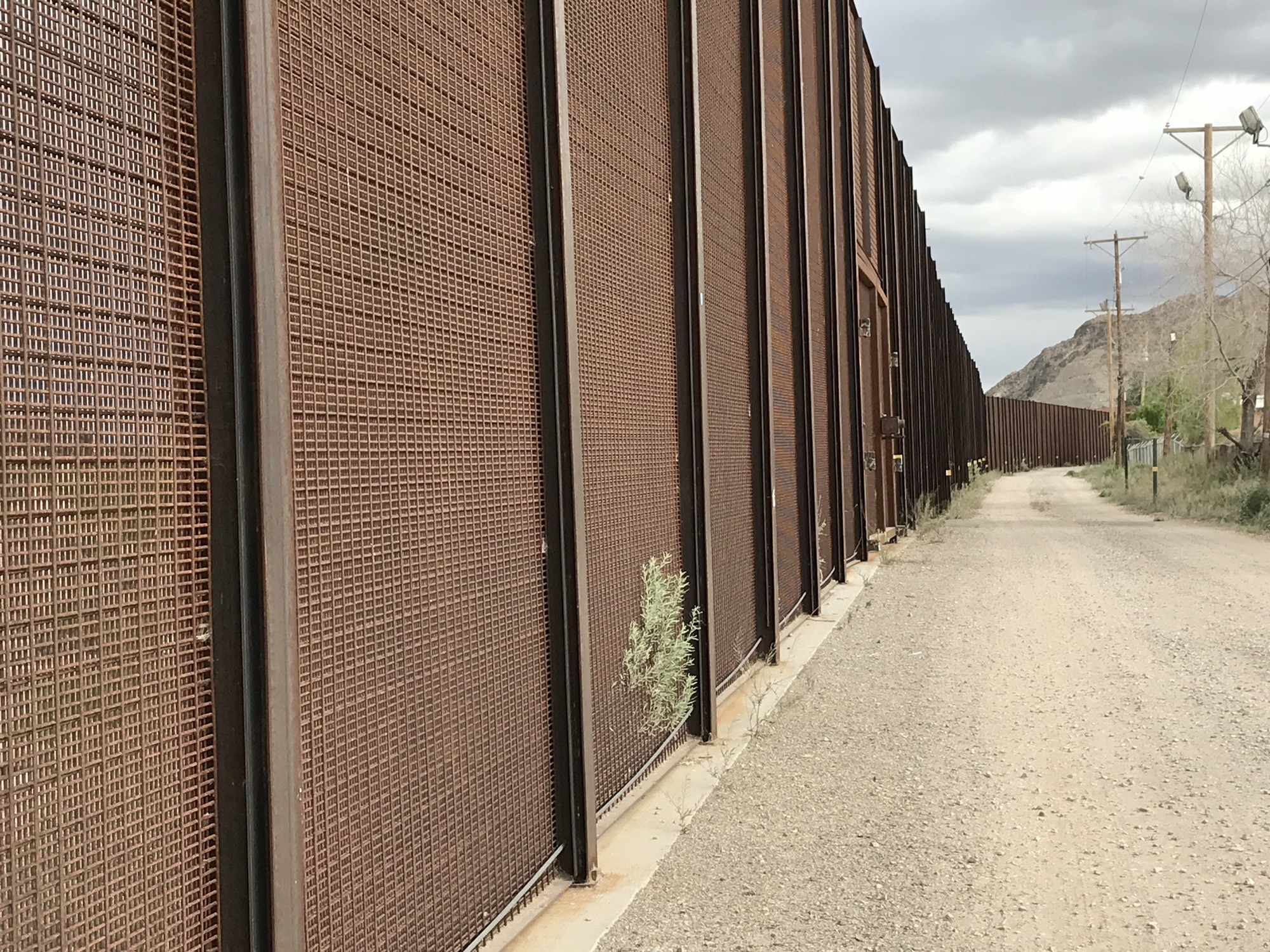 A dirt road next to a border wall.