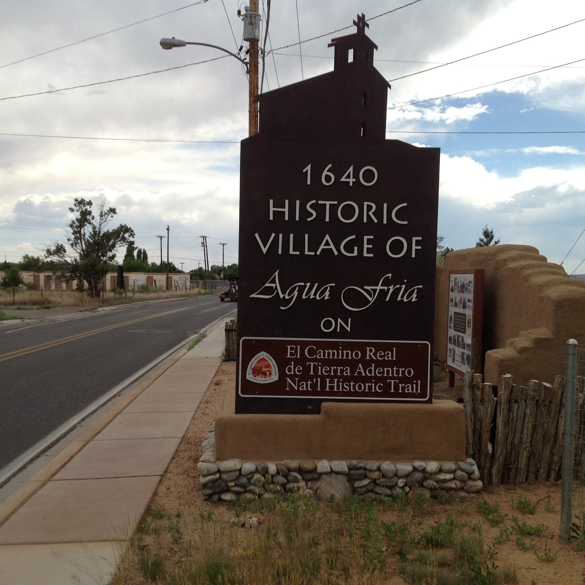 A sign with text "Historic Village of Agua Fria" on it beside a road.