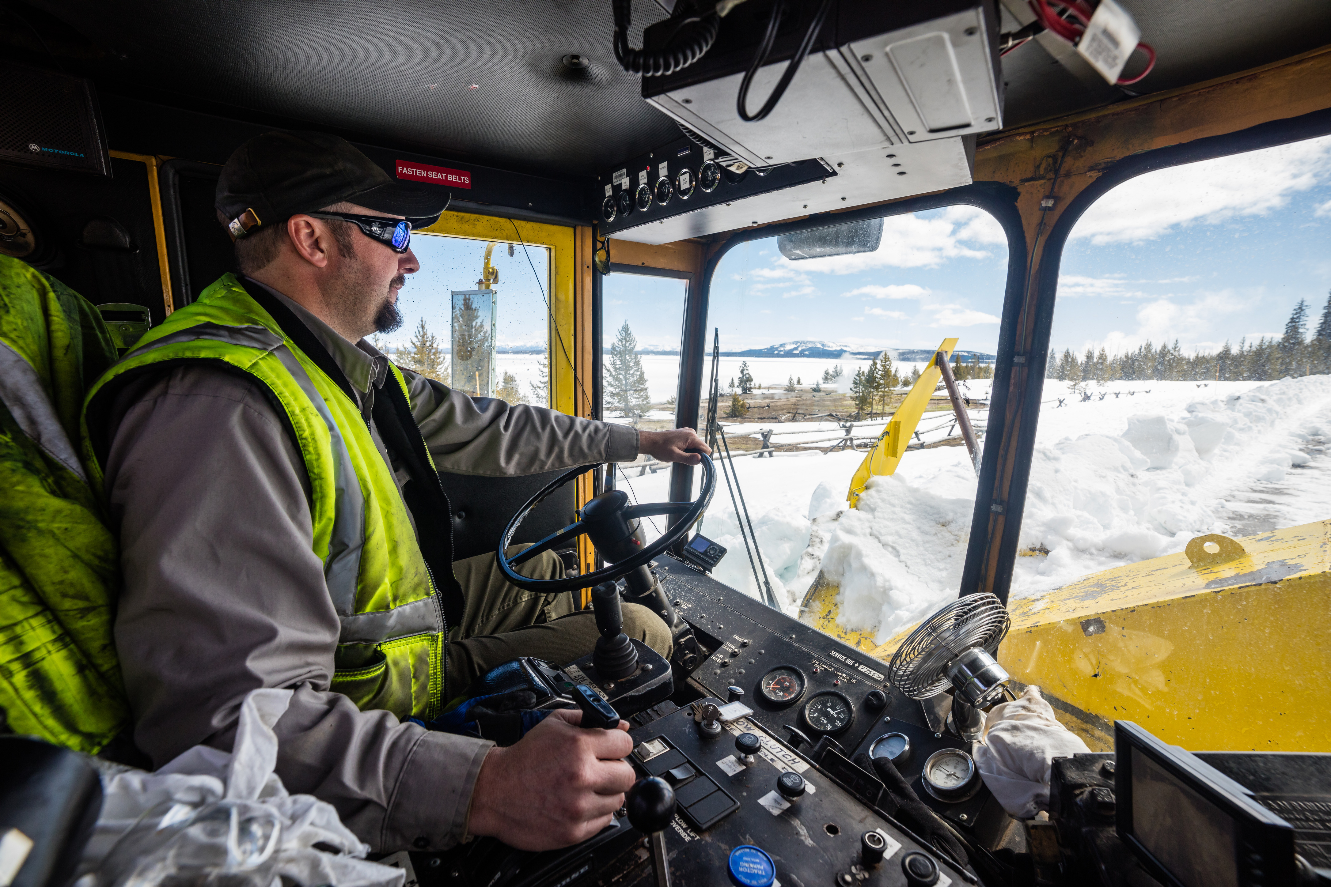 Looking inside the cab of a large rotary blower with the driver operating it.