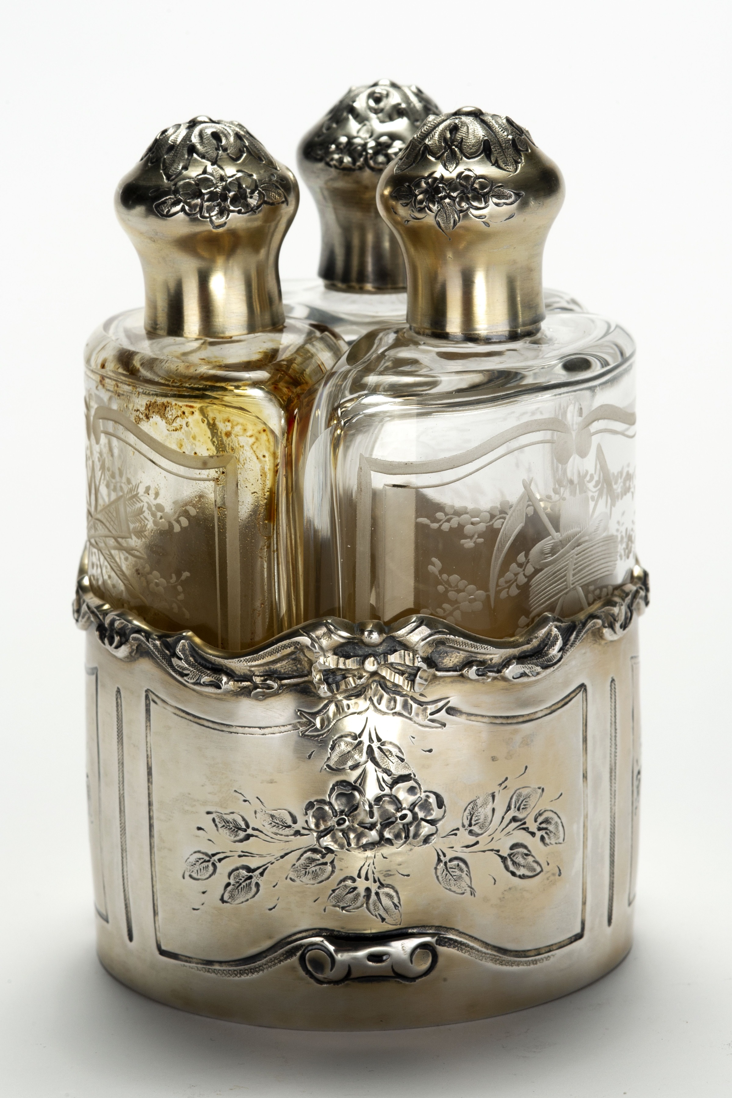 A floral engraved silver container with three curved etched glass containers and silver caps.
