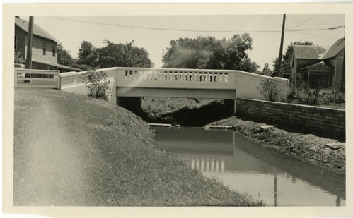A 1931 photo depicts a concrete bridge spanning a small town creek.