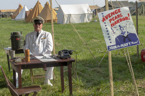 A reenactor in a naval uniform seated behind a recruiting table.