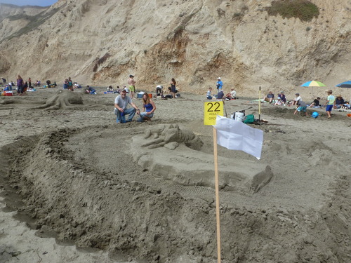A sand sculpture with a wolf lying on the north end of a platform in the shape of California.