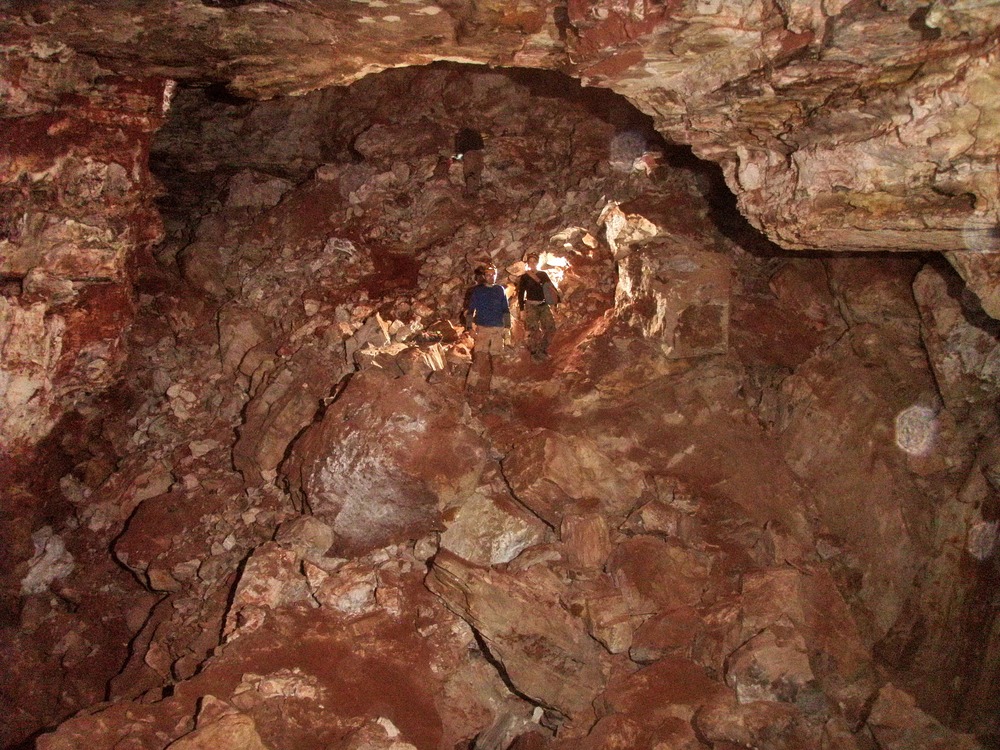 three small cavers standing on a pile of boulders in a very large cave room
