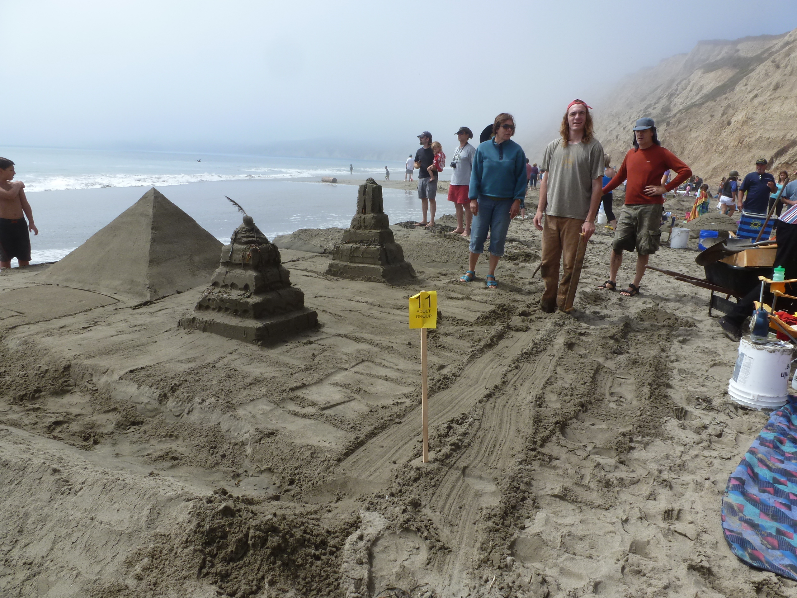 A large sand sculpture of three pyramids, two of which have terraced sides.