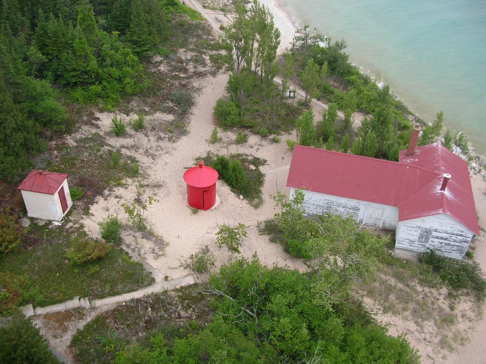 An aerial view of a T shaped building with a bright red roof and white siding. To the left of the building is a small red cylindrical building.