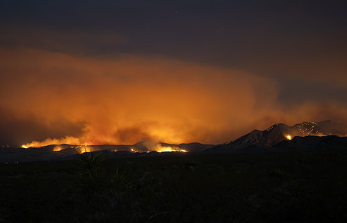 Wildfire and smoke are lit up in orange on a mountainside at night
