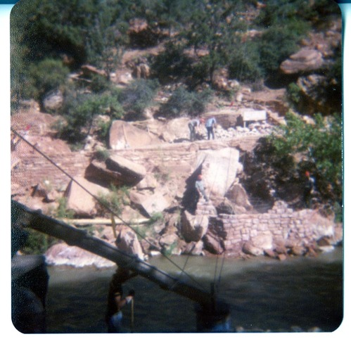 Men building stone abutment for the new Grotto footbridge, woman guiding cement chute for other abutment in foreground.