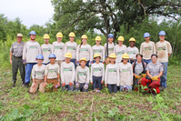 Twelve Youth and six leaders stand in a double row outdoors with three park rangers in uniform 