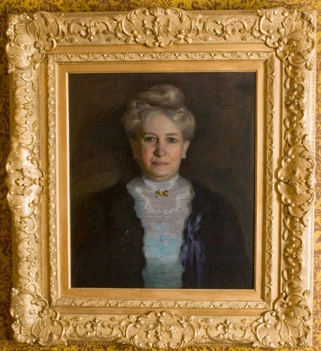 Portrait of older woman seated facing front, gray hair arranged on top of head, wearing lace blouse and dark blue jacket