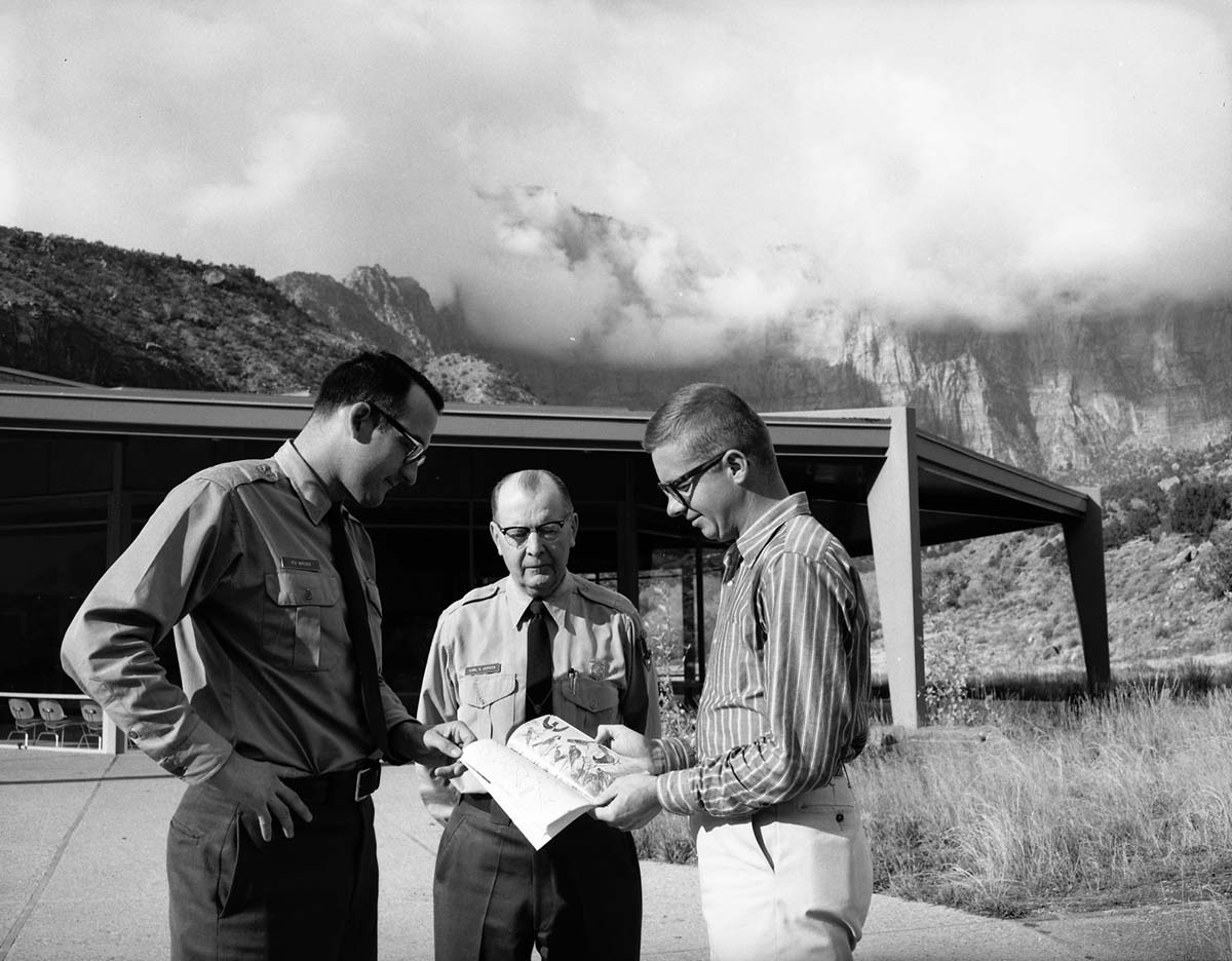Chief Naturalist Carl E. Jepson (center) stands in front of Mission 66 Visitor Center and Museum with Ranger Roland H. Wauer (left) and Dennis Carter, authors of the 'Birds of Zion' guide book.
