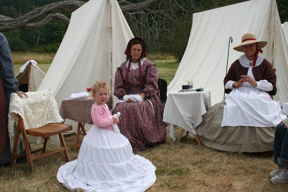 A little girl tries on a hoop skirt under the watchful eye of NPS volunteers Anne Lorgen and Kathy Wieck.