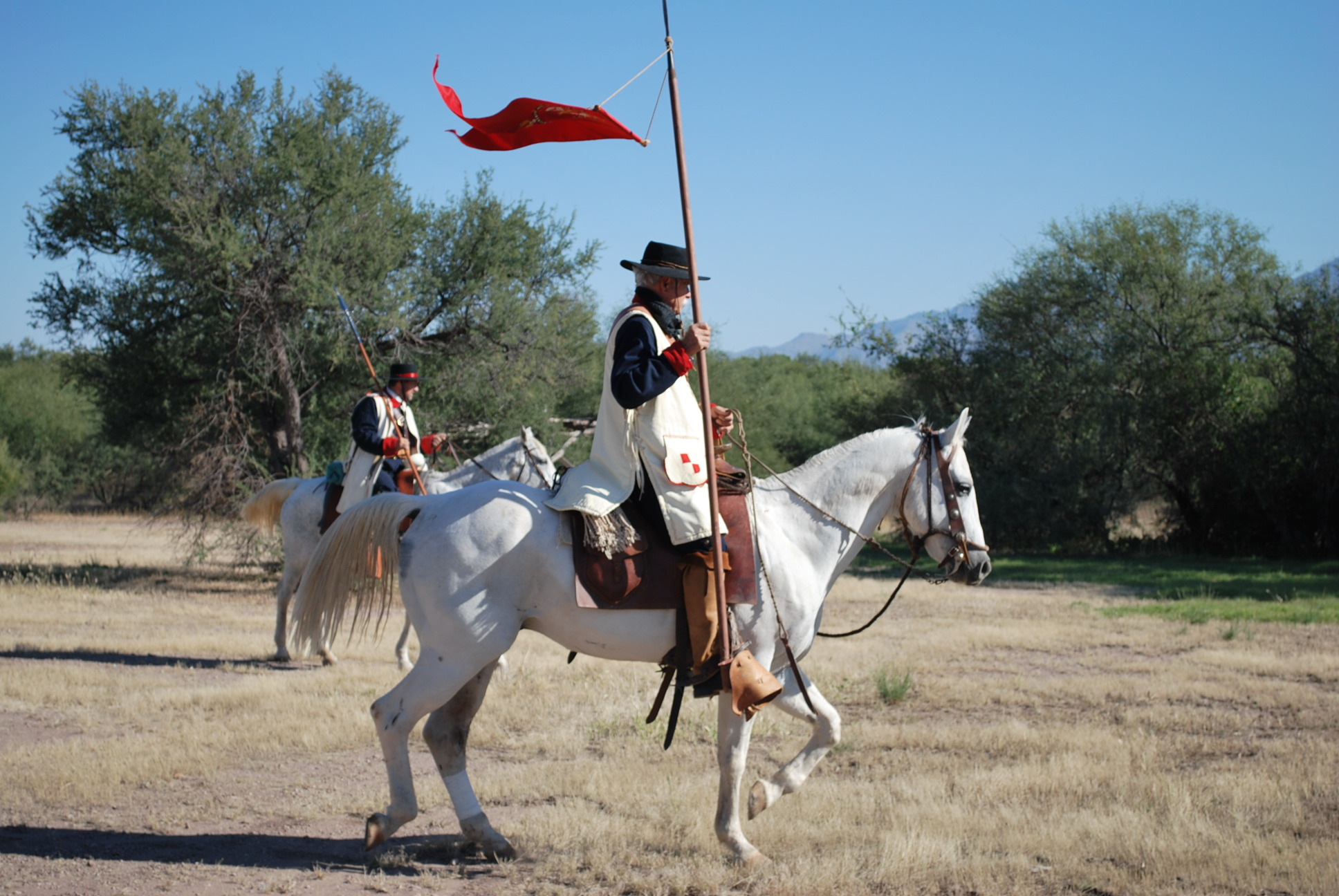 A person wearing Spanish colonial clothing carries a flag on horseback