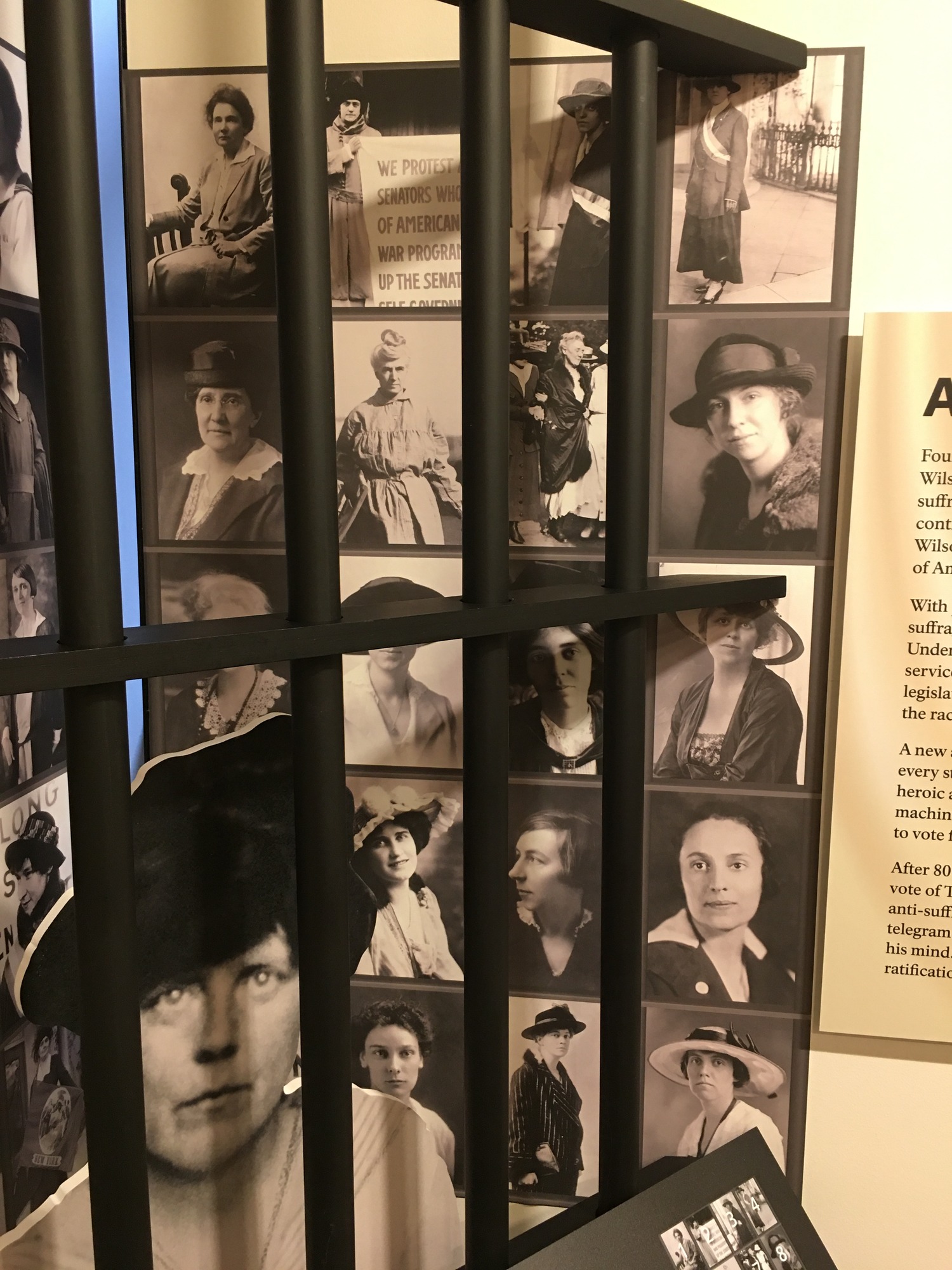 A zoomed in photo of the right side of women's photos behind a Lucy Burns cut out and prison bars. 