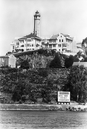 Alcatraz from the bay with "Indian Property" sign at shoreline and lighthouse and buildings above