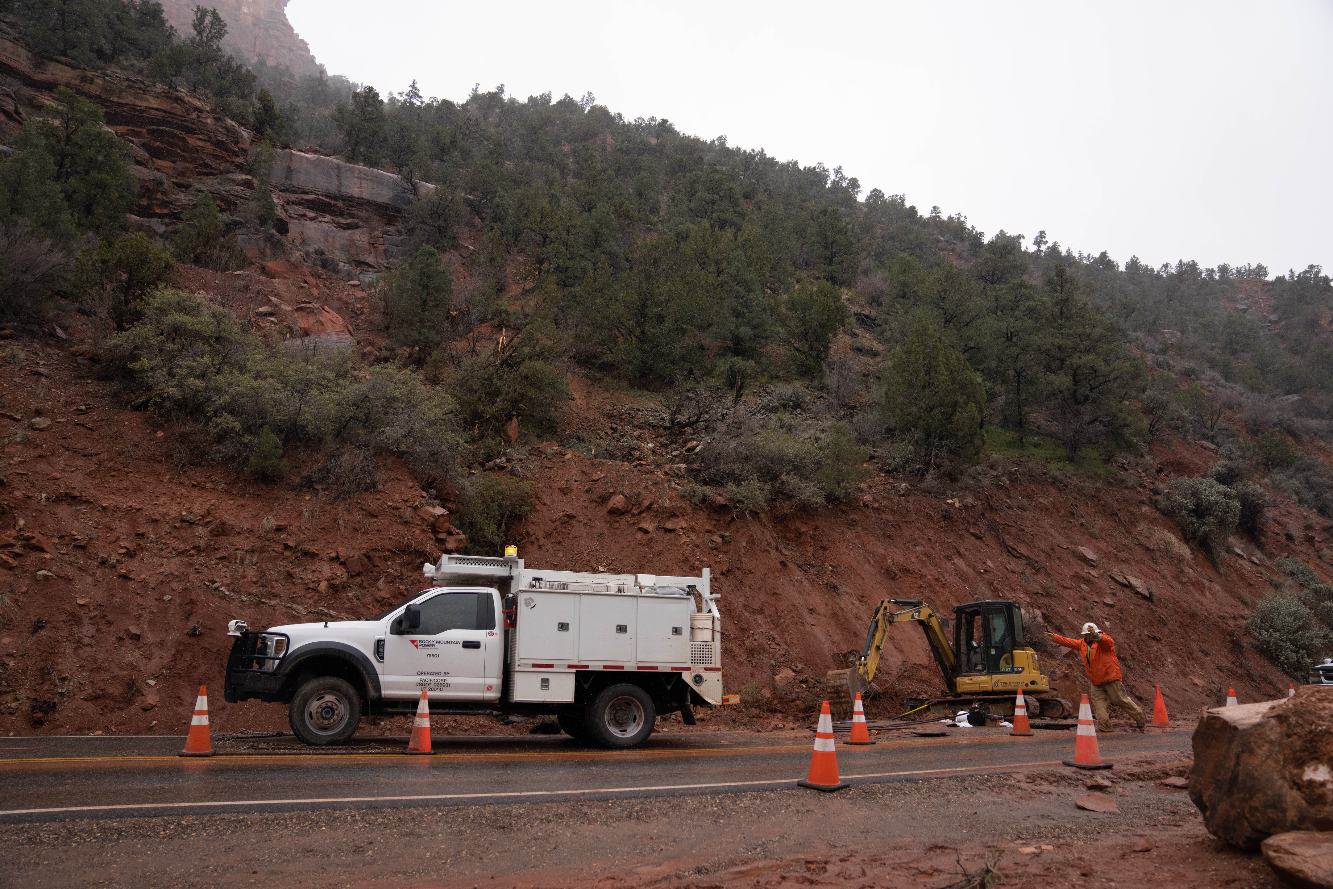 A worker directs traffic next to an electric truck and a large hole closing one lane.