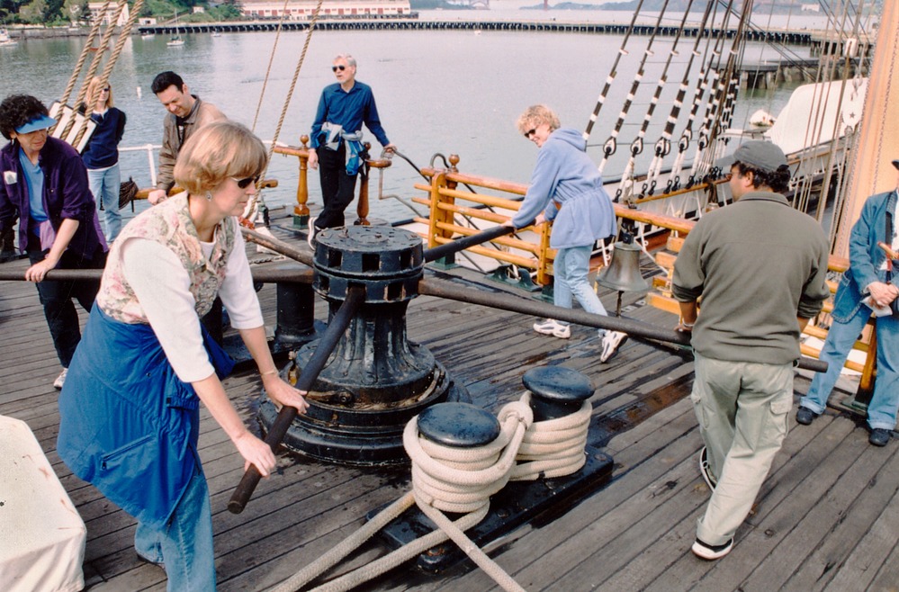 Visitors holding wooden bars and walking around a winch.