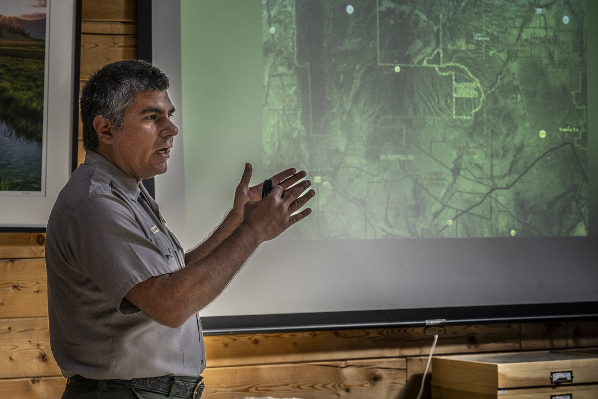 A man stands in front of a projected slideshow and speaks to a seated audience.