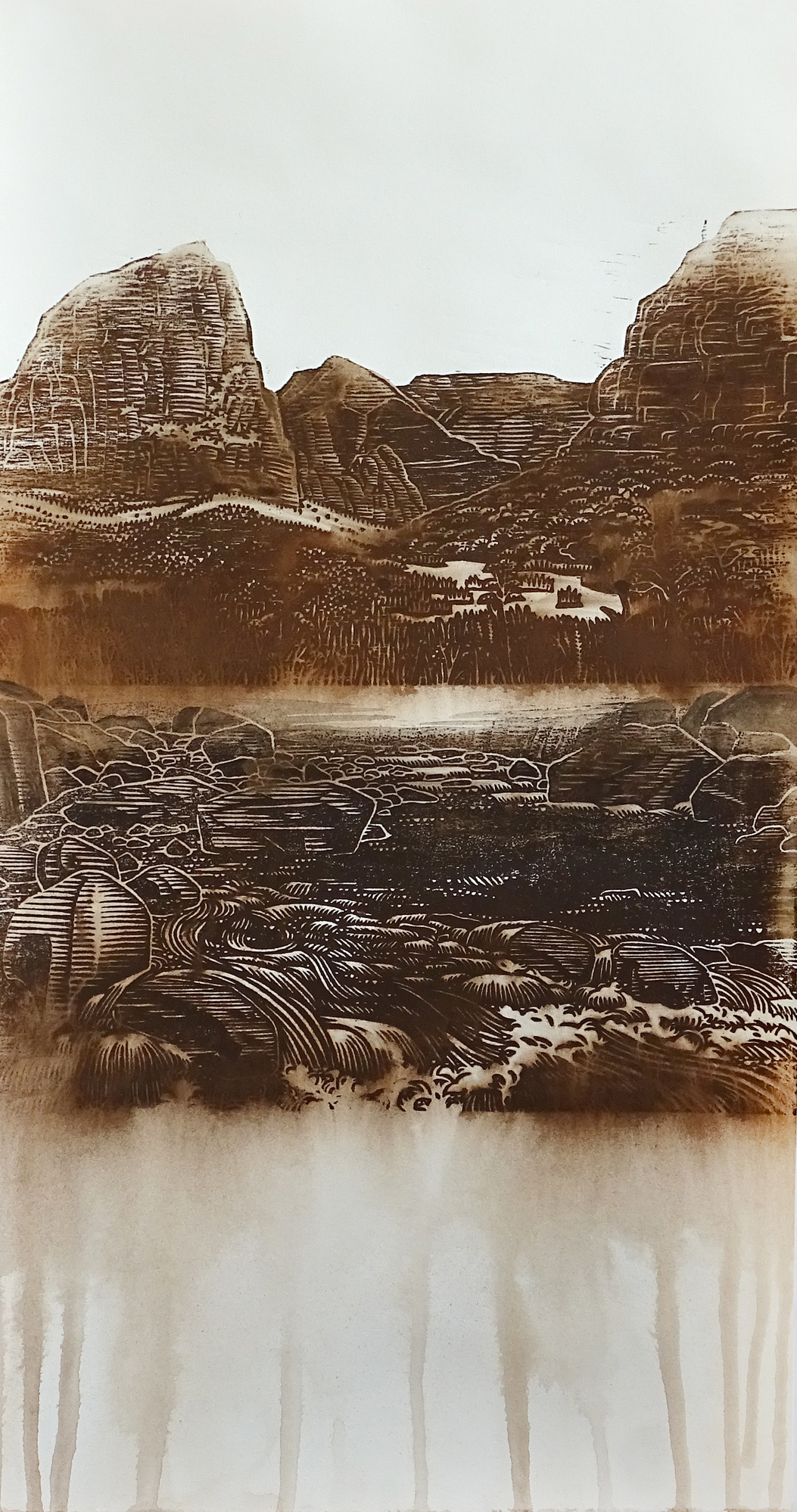 A texture-rich monochrome image printed on paper using woodblock printing. In the foreground, water flows through a boulder-covered canyon floor, creating pools and rapids. In the middleground, a grassy field blends into a shrub-covered hillside. A rocky cliff face is seen above the hill. Behind the field and cliff, a large sandstone peak stands above surrounding vegetation. In the background, tall flat-topped cliffs stand before a white sky.