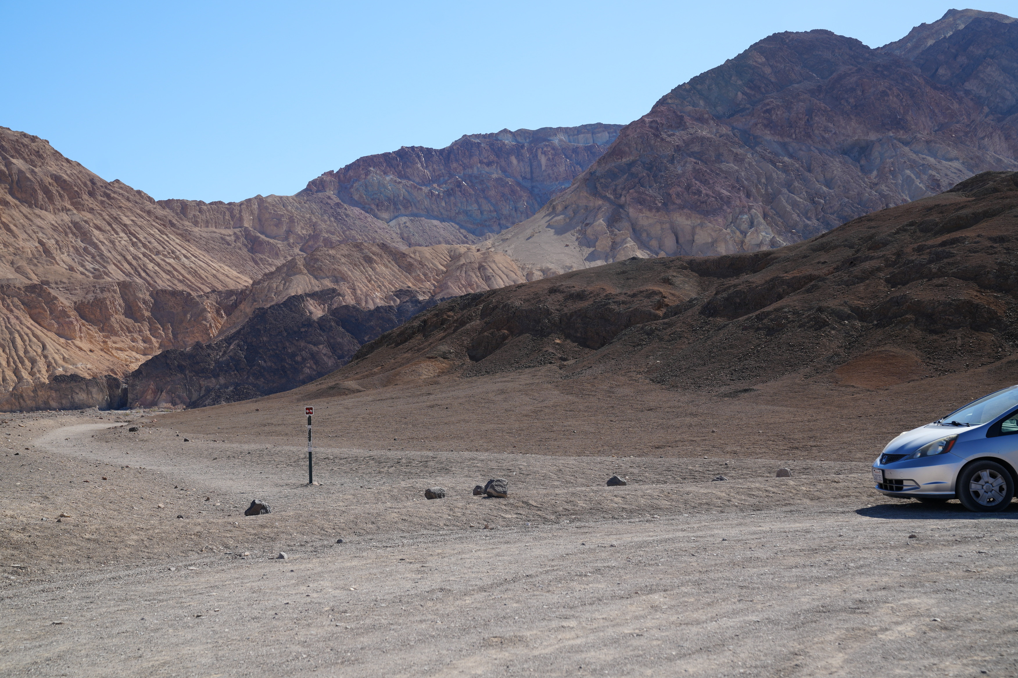 Desolation Canyon trailhead. A post marks the trailhead. The gravel parking lot is right in front of the trailhead. The trail is largely gravel and wraps towards the mouth of a canyon.