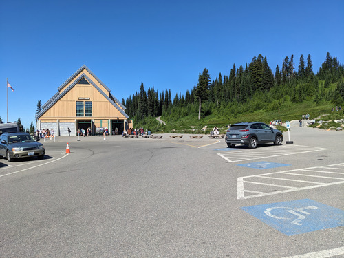 A large parking lot showing three of the accessible parking spaces and level paved area in front of a toffee-colored A-frame building.