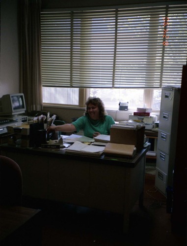 Color Photos of administration personnel. Woman seated at desk.