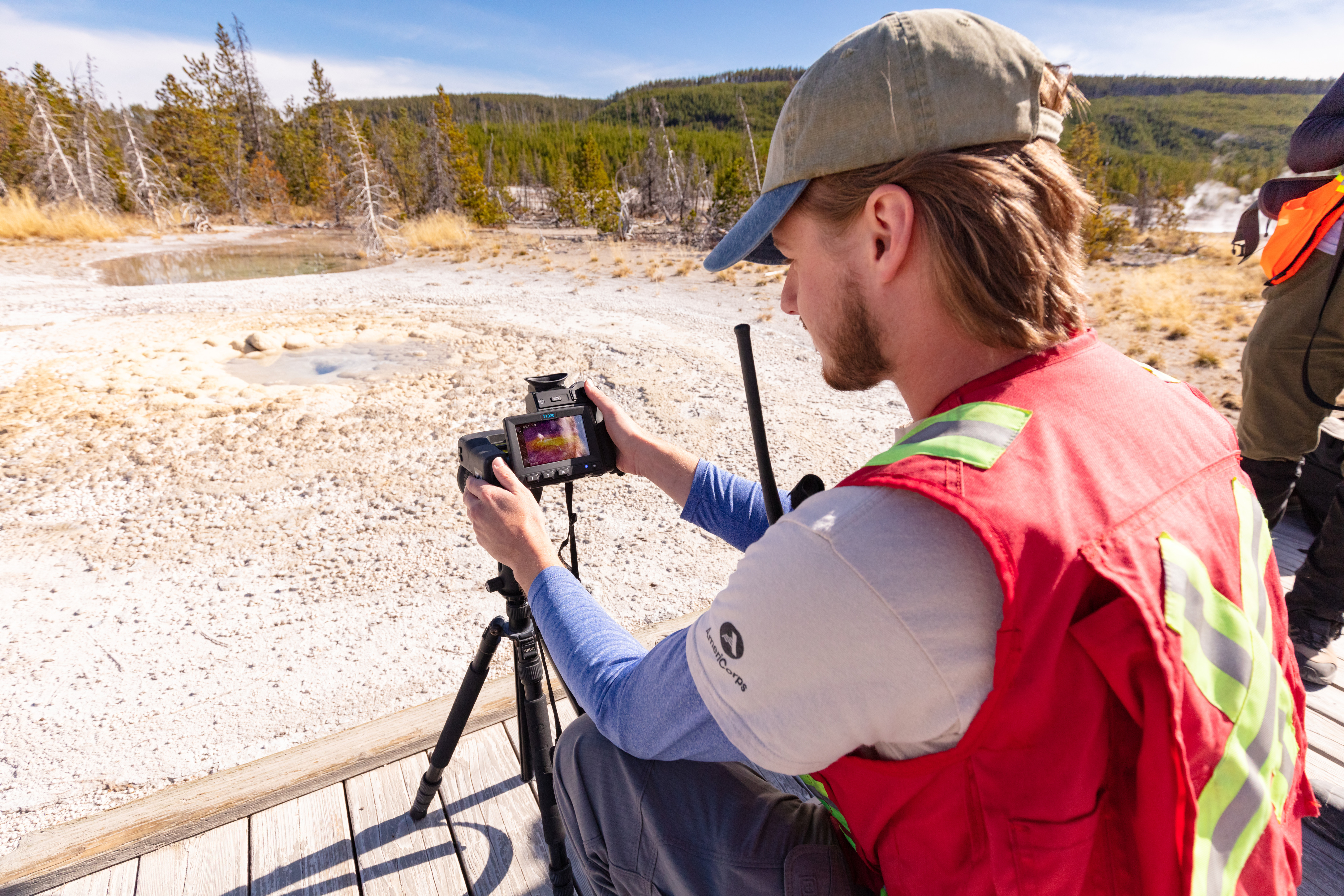 A man looks at a camera screen on the boardwalk in a geyser basin