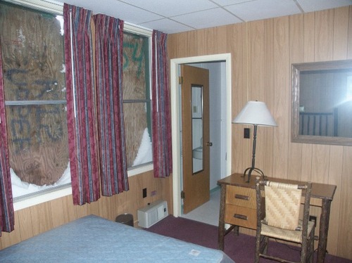 An interior of a room with dark wood siding on the walls, maroon carpet and drapes, and wood-log furniture.