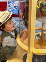 A small child looks into a clear tube, with a parachute inside. 