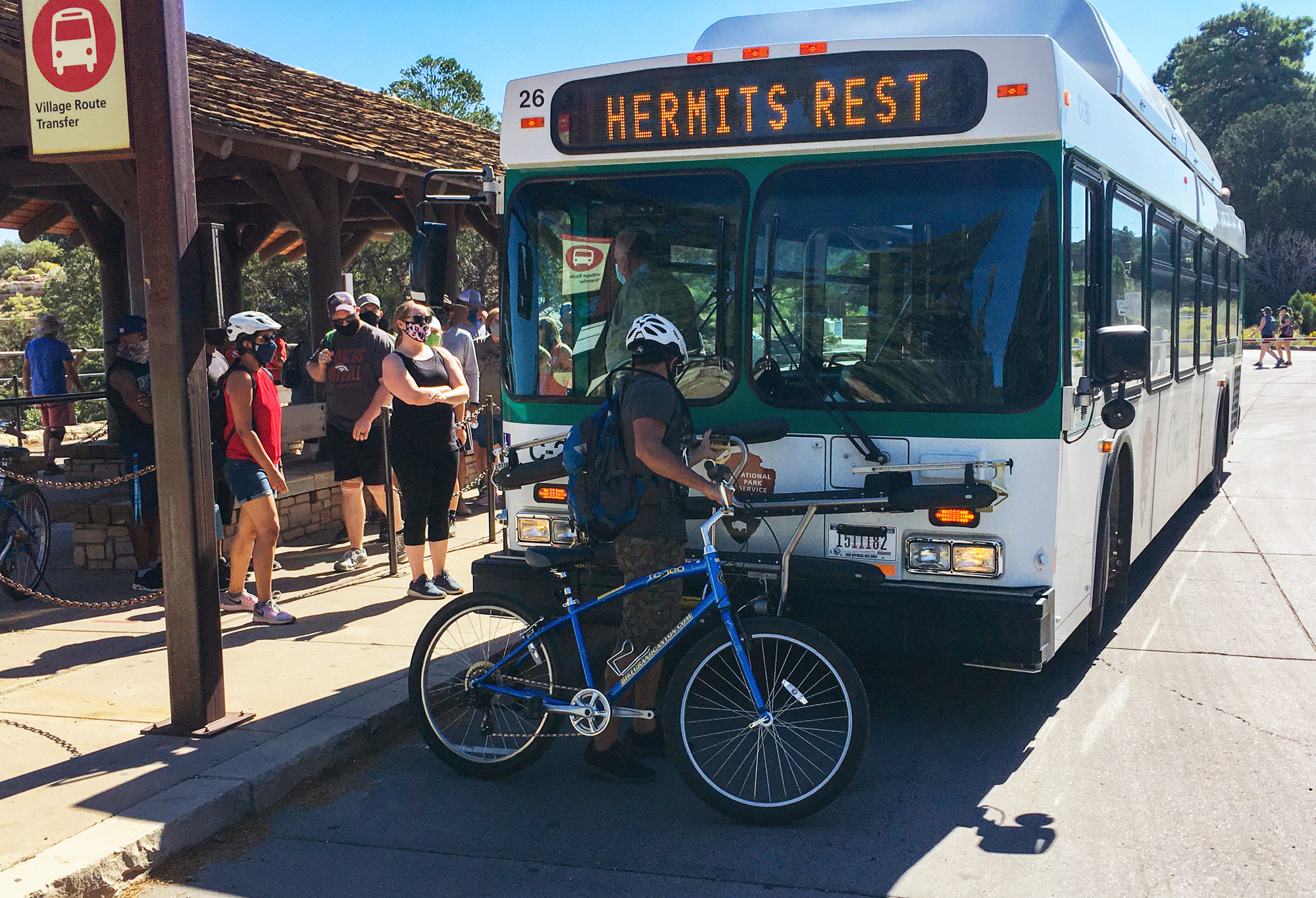 a person about to load a bicycle onto the front bicycle rack of a large bus.