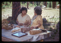 Two women stand in front of a display of Atsugewi crafts.