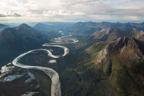 a river snakes its way through a valley surrounded by tall green craggy peaks 