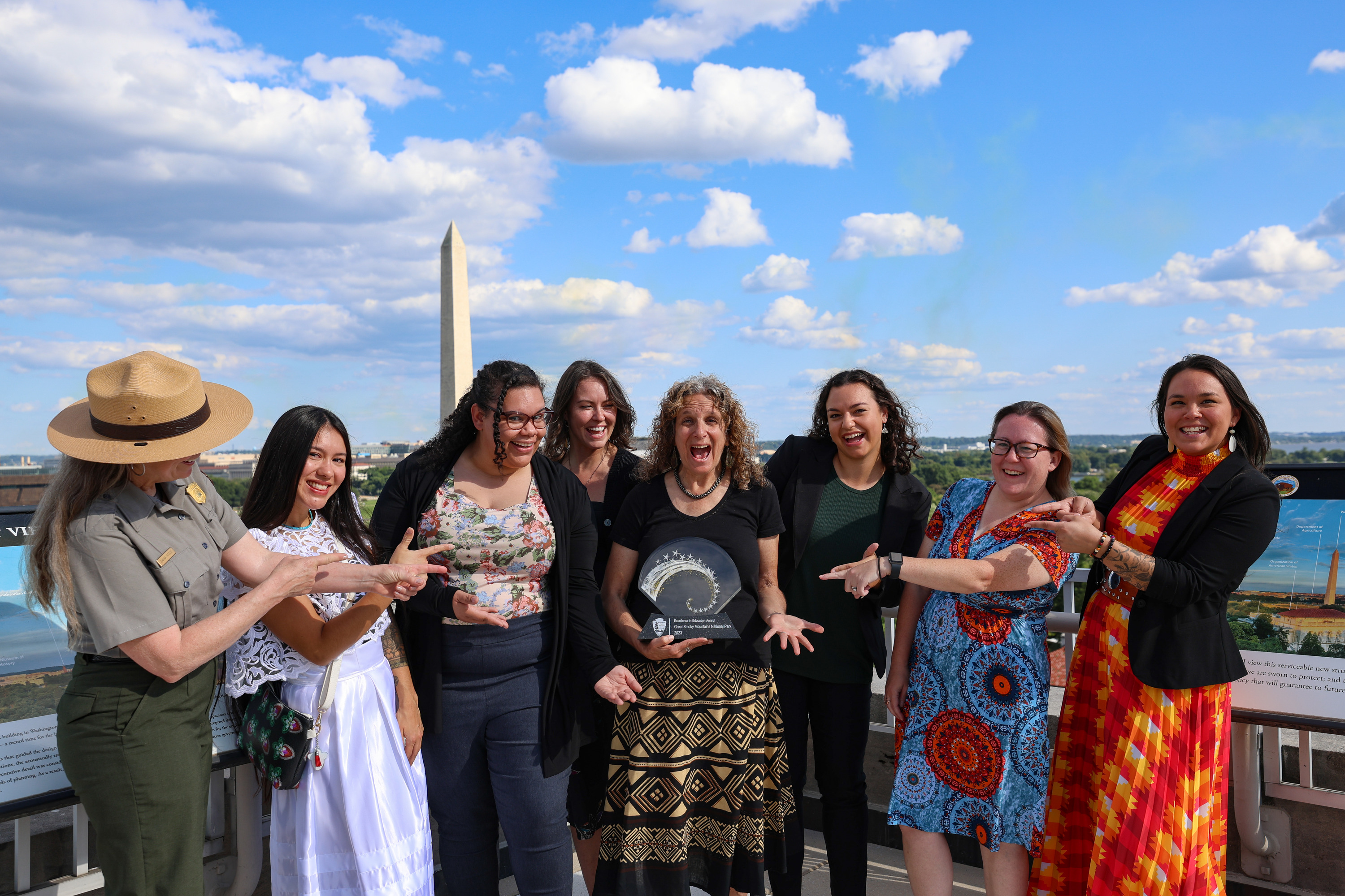 Seven female award recipients and a park ranger pose for a photo on a rooftop.