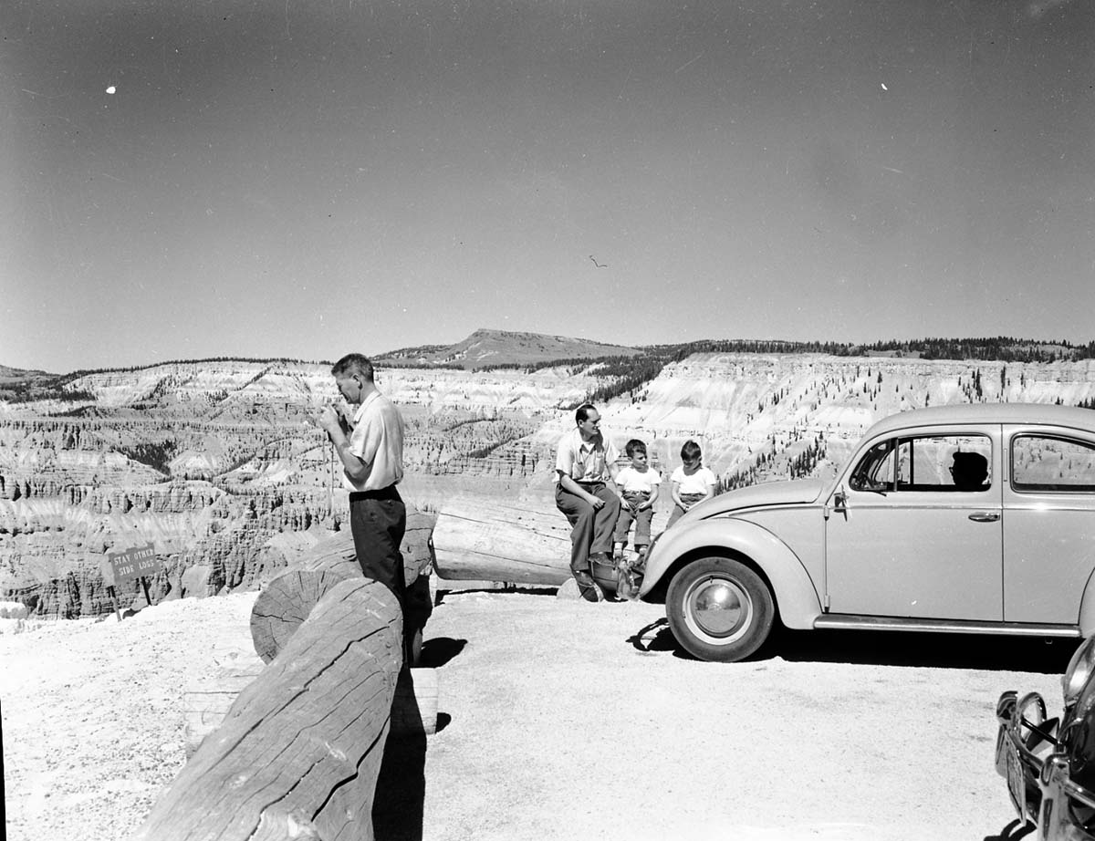 Visitors and children at Point Supreme, Volkswagen Beetle and car parked on rim. Sign reads: Stay Other Side Logs.